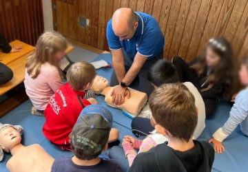 eine Gruppe Kinder sieht dem Trainer bei der Reanimation zu